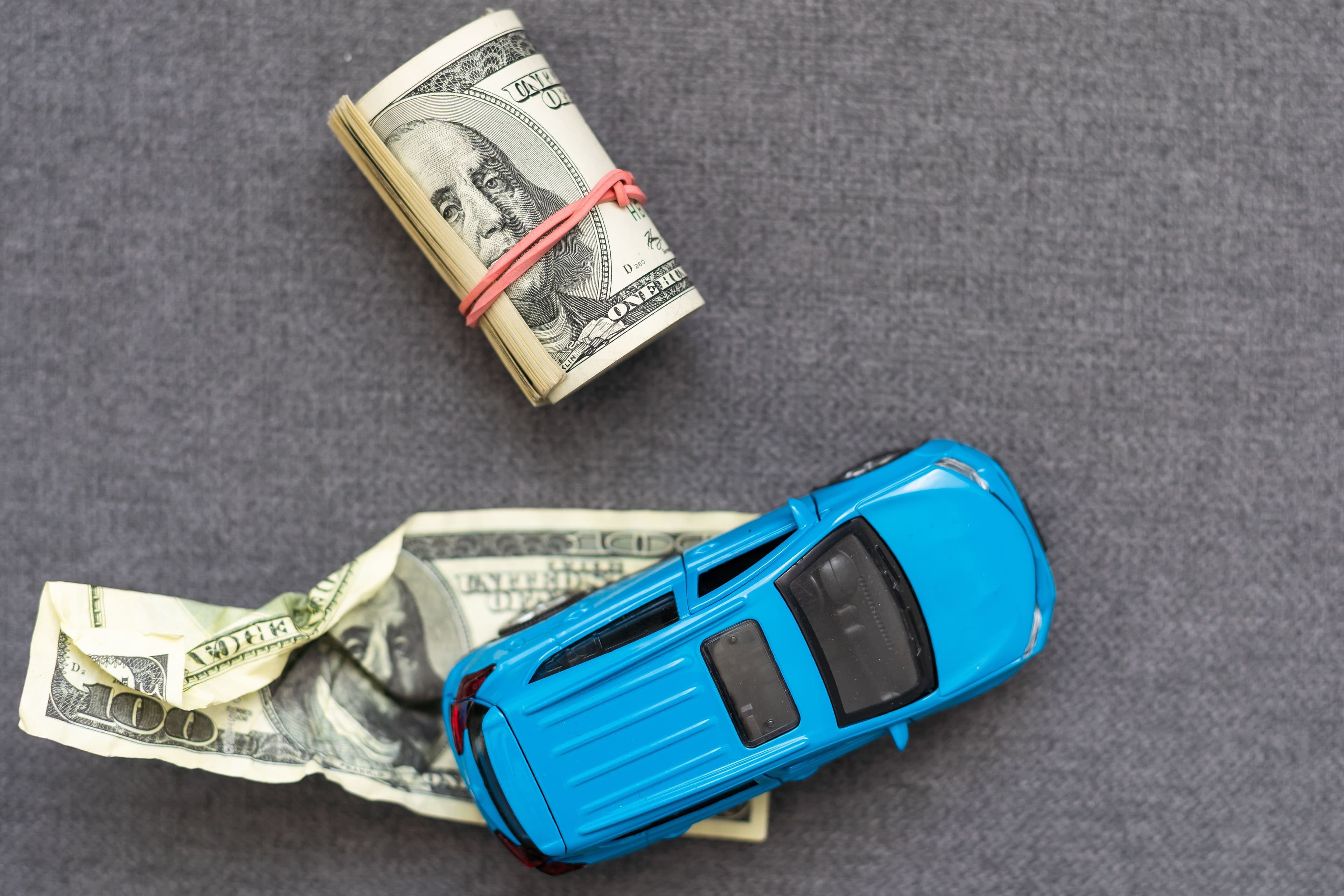 A toy car driving over a crumpled dollar bill, illustrating how easily car accidents lead to financial hardship.