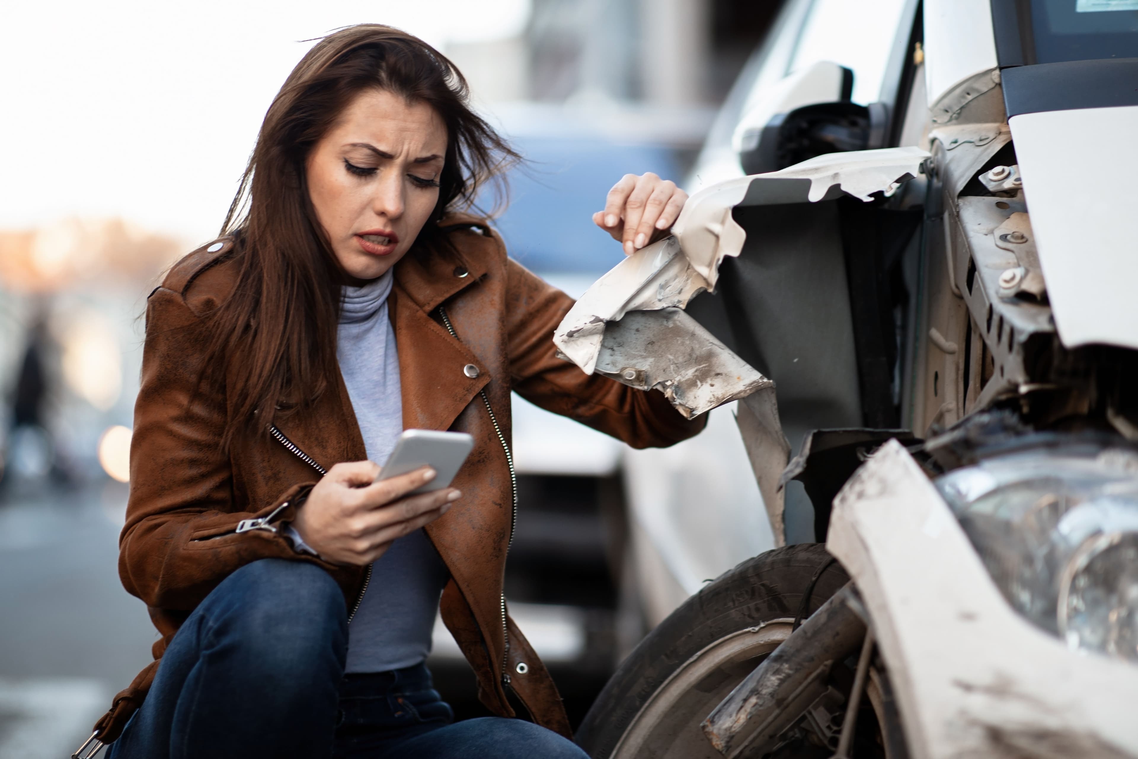 A driver checking her phone by her car after an Uber accident. Uber’s liability insurance hinges on the app’s ride status.
