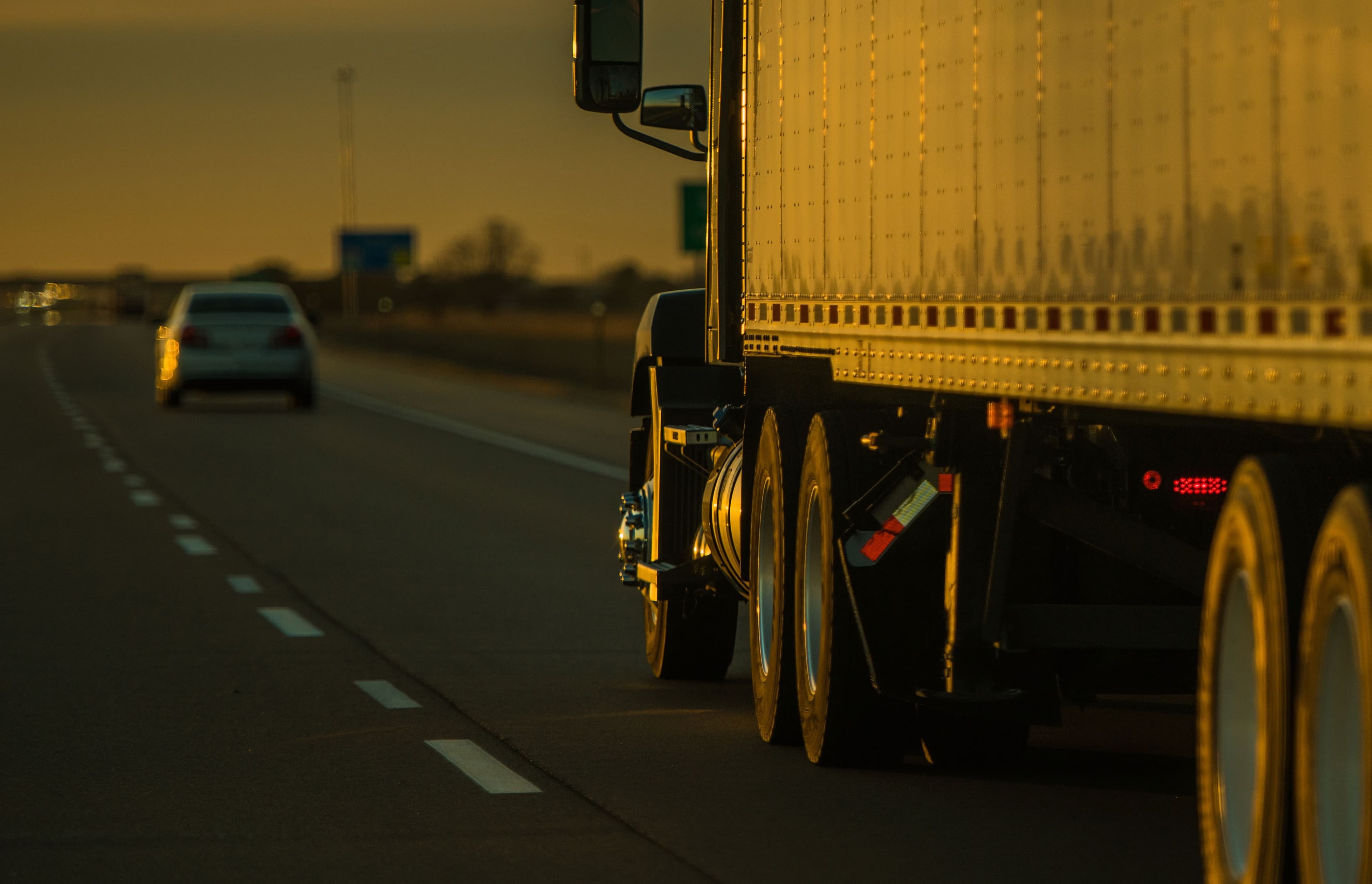 Rear view of a large truck on the road at dusk, behind a sedan.