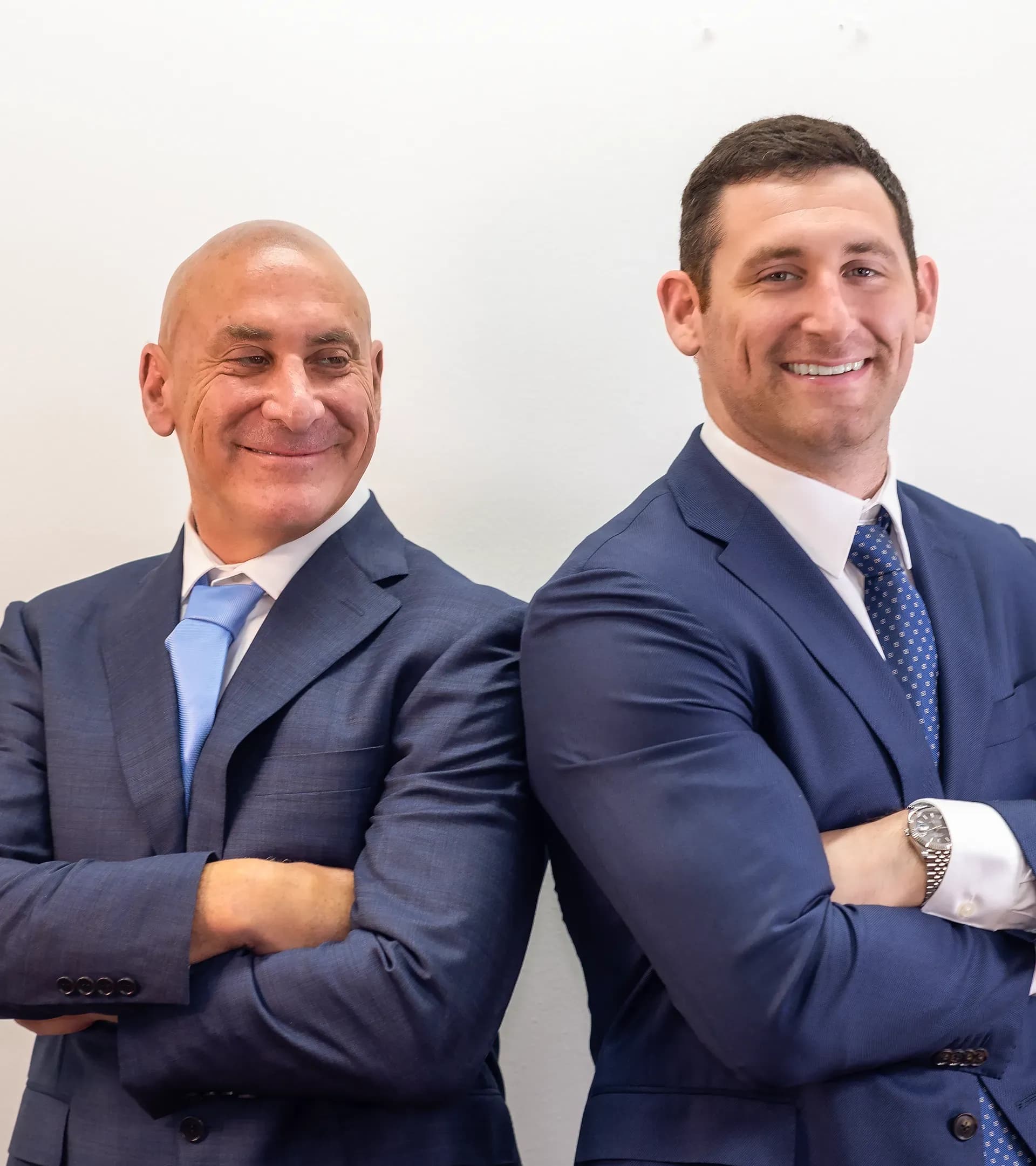 Personal injury attorneys Scott and Alex Senft standing back to back and smiling with arms crossed.
